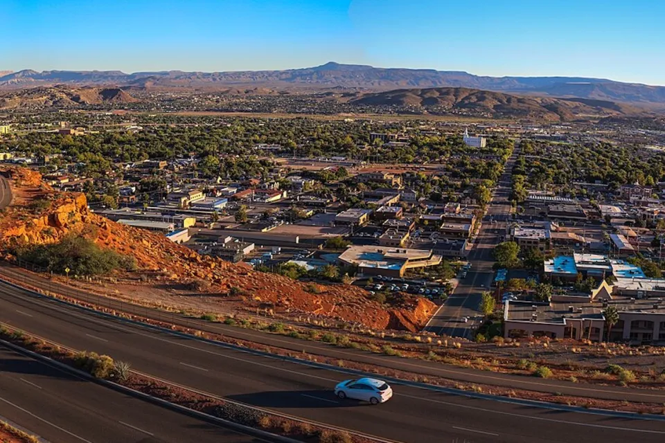 Aerial view of St. George, Utah at sunset with road in foreground and red mountains in background.
